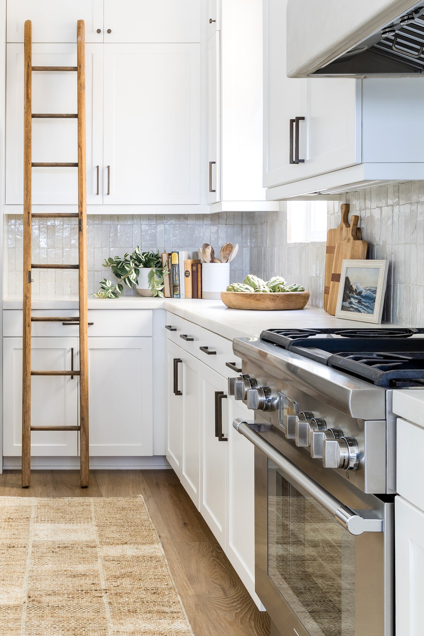 Modern farmhouse kitchen: white shaker cabinets, stainless range, natural wood ladder, light wood floors, woven rug.