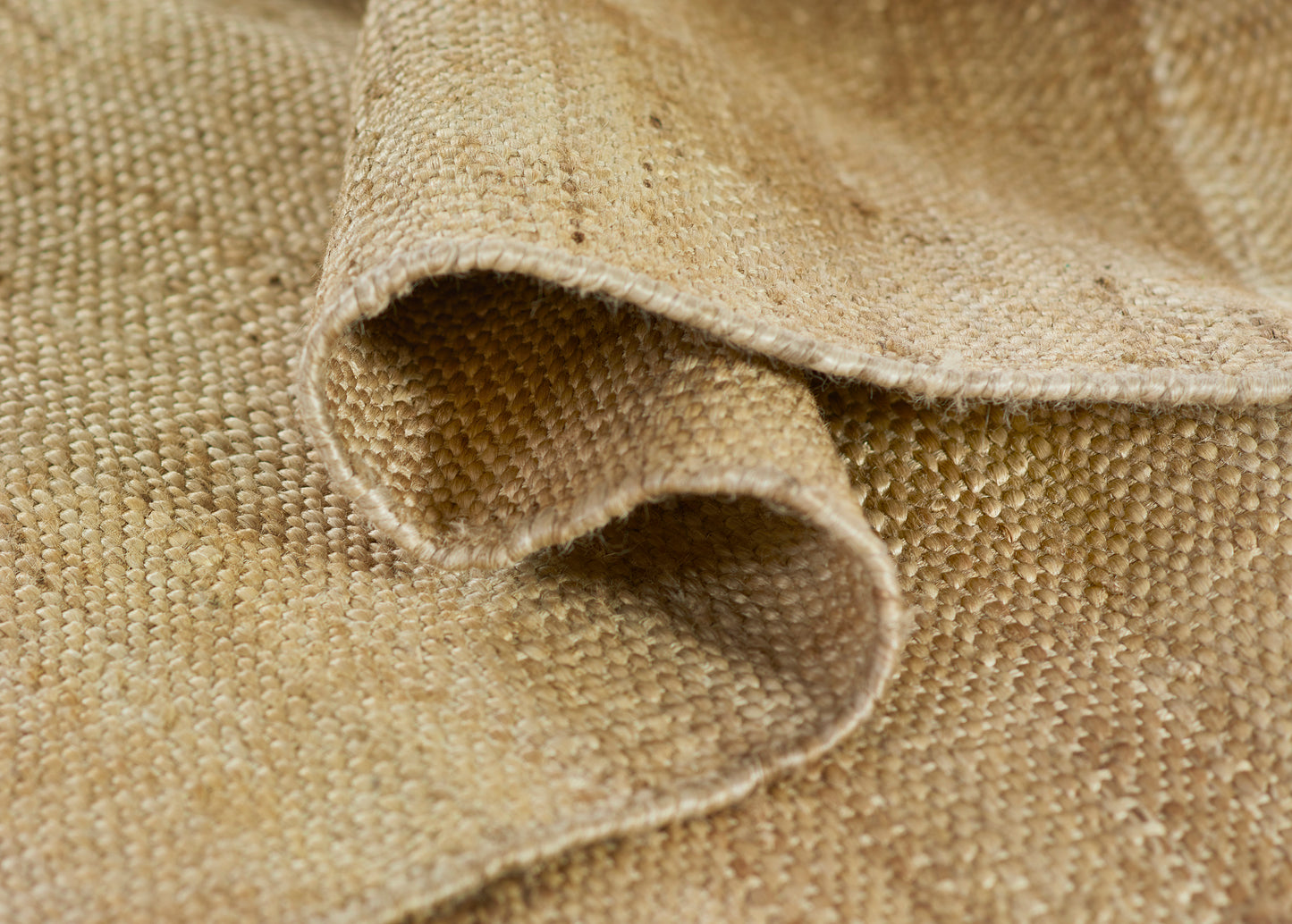 Natural beige burlap-style rug close-up with folded edges, coarse woven jute texture.