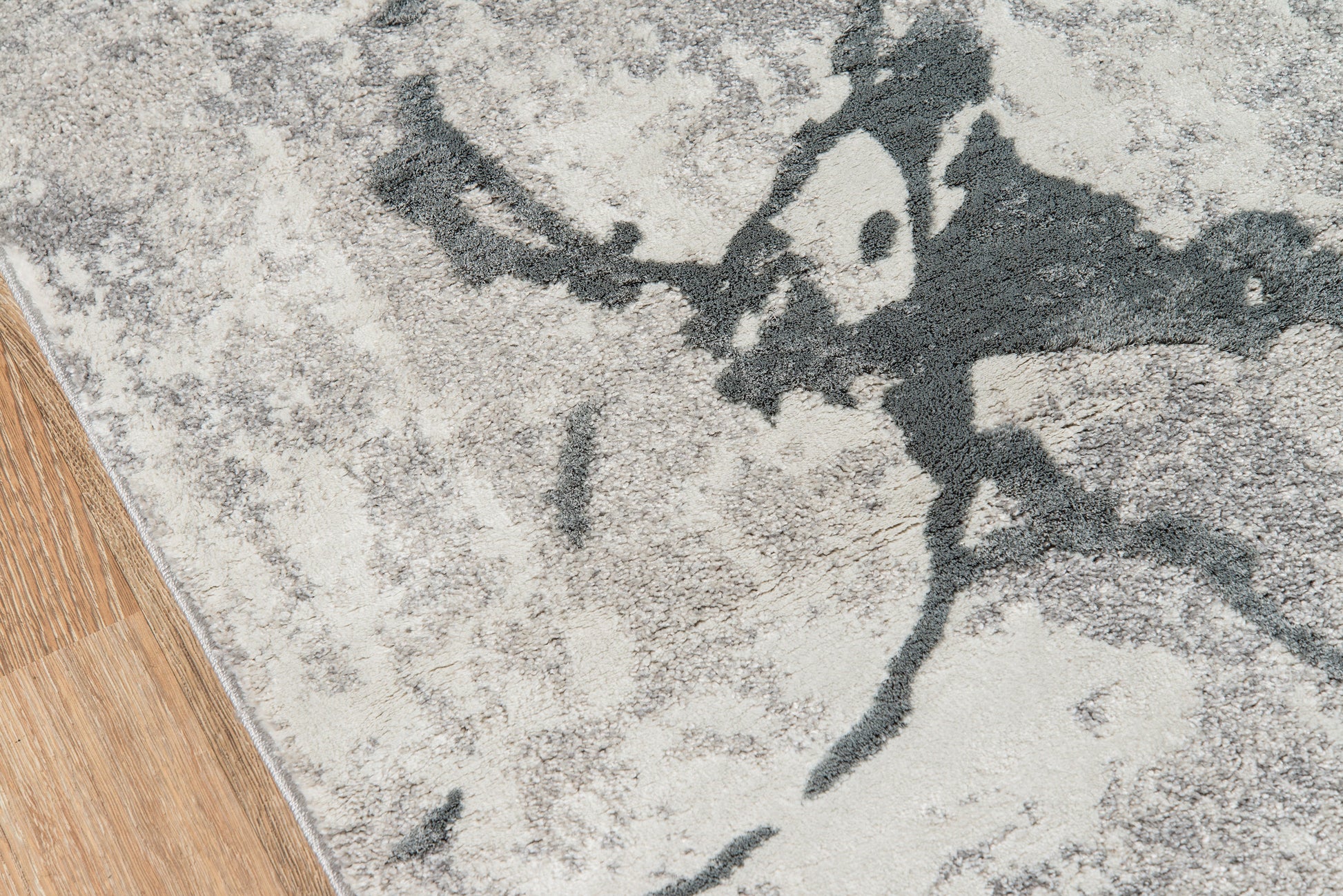 Abstract gray area rug with dark charcoal marbling on a light beige field, lying on wood flooring.