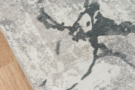 Abstract gray area rug with dark charcoal marbling on a light beige field, lying on wood flooring.