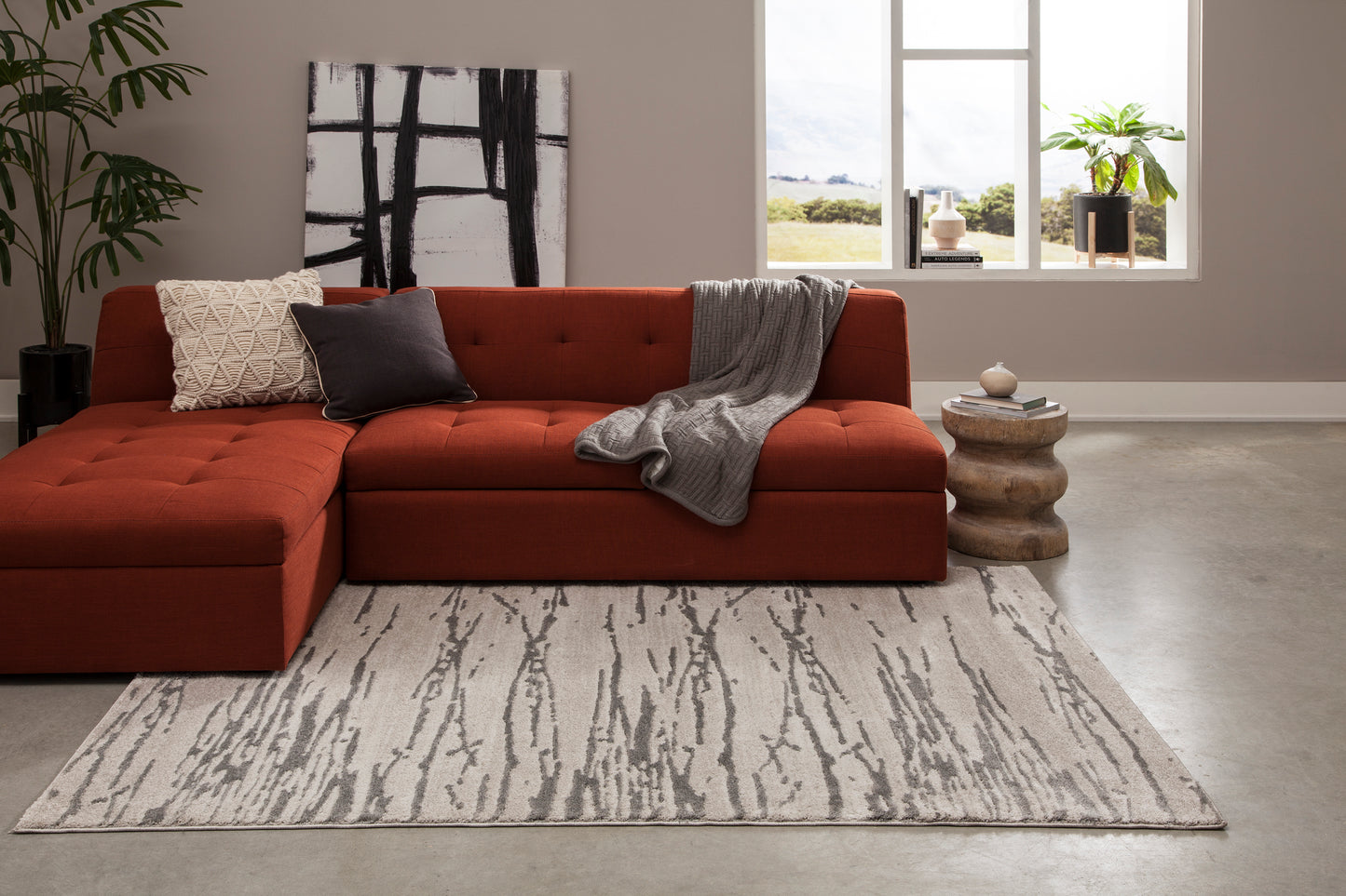 Rectangular gray area rug with bold abstract charcoal lines, styled beneath an orange sectional sofa in a modern living room.