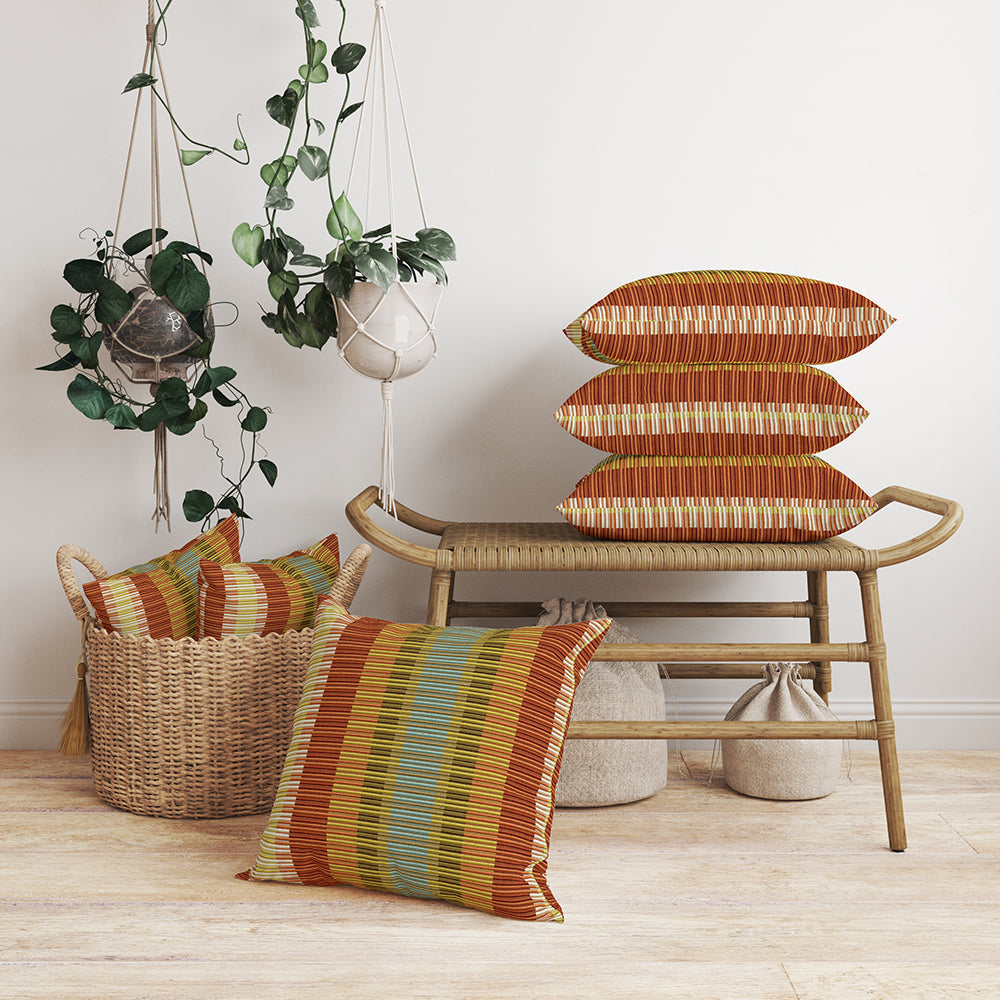 Boho living room scene featuring Canyon Stripe fabric on cushions; orange-striped cushions on a rattan bench, wicker basket of cushions, hanging planters and soft poufs.