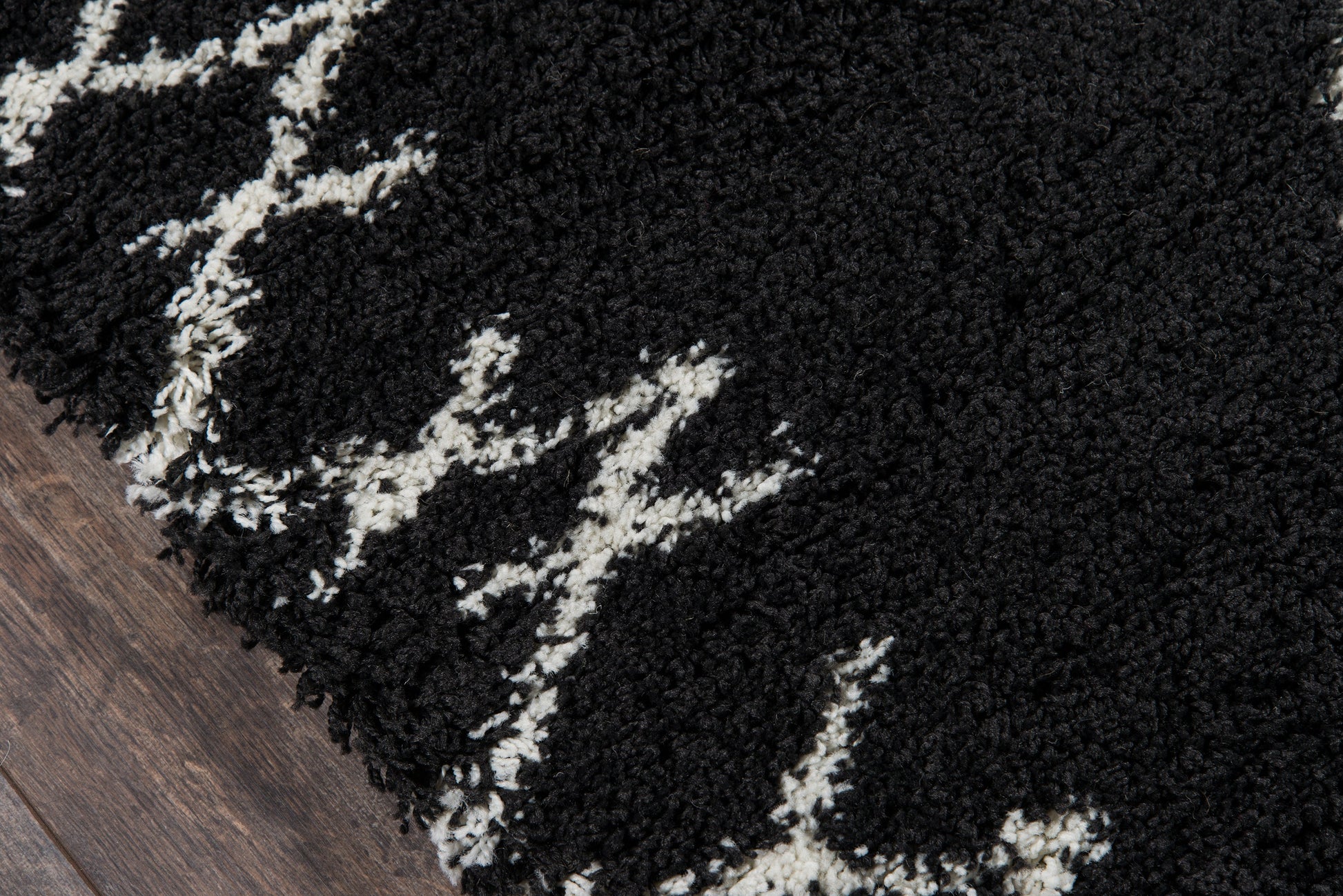 Black shag rug with white abstract lines and thick pile on a wooden floor.
