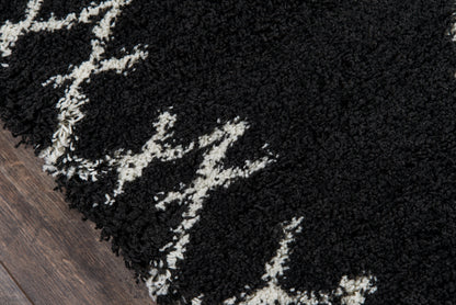 Black shag rug with white abstract lines and thick pile on a wooden floor.