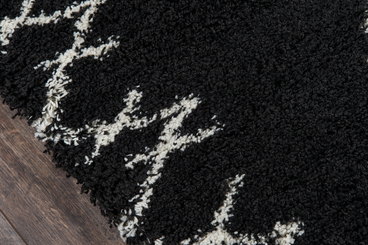 Black shag rug with white geometric line pattern, plush high-pile texture on dark wood floor.