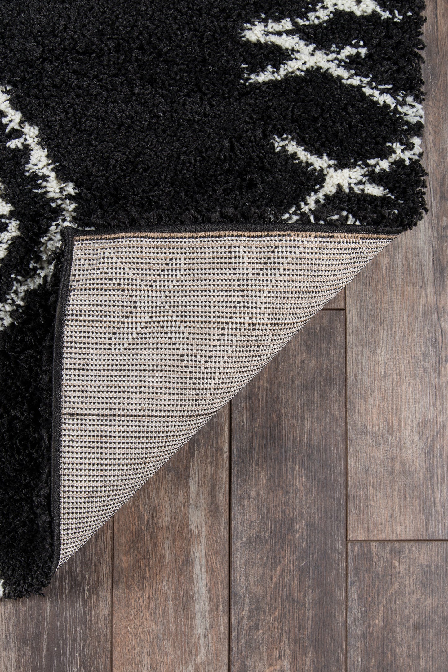 Black shag rug with white geometric pattern; folded back to show beige grid underside on wood floor.