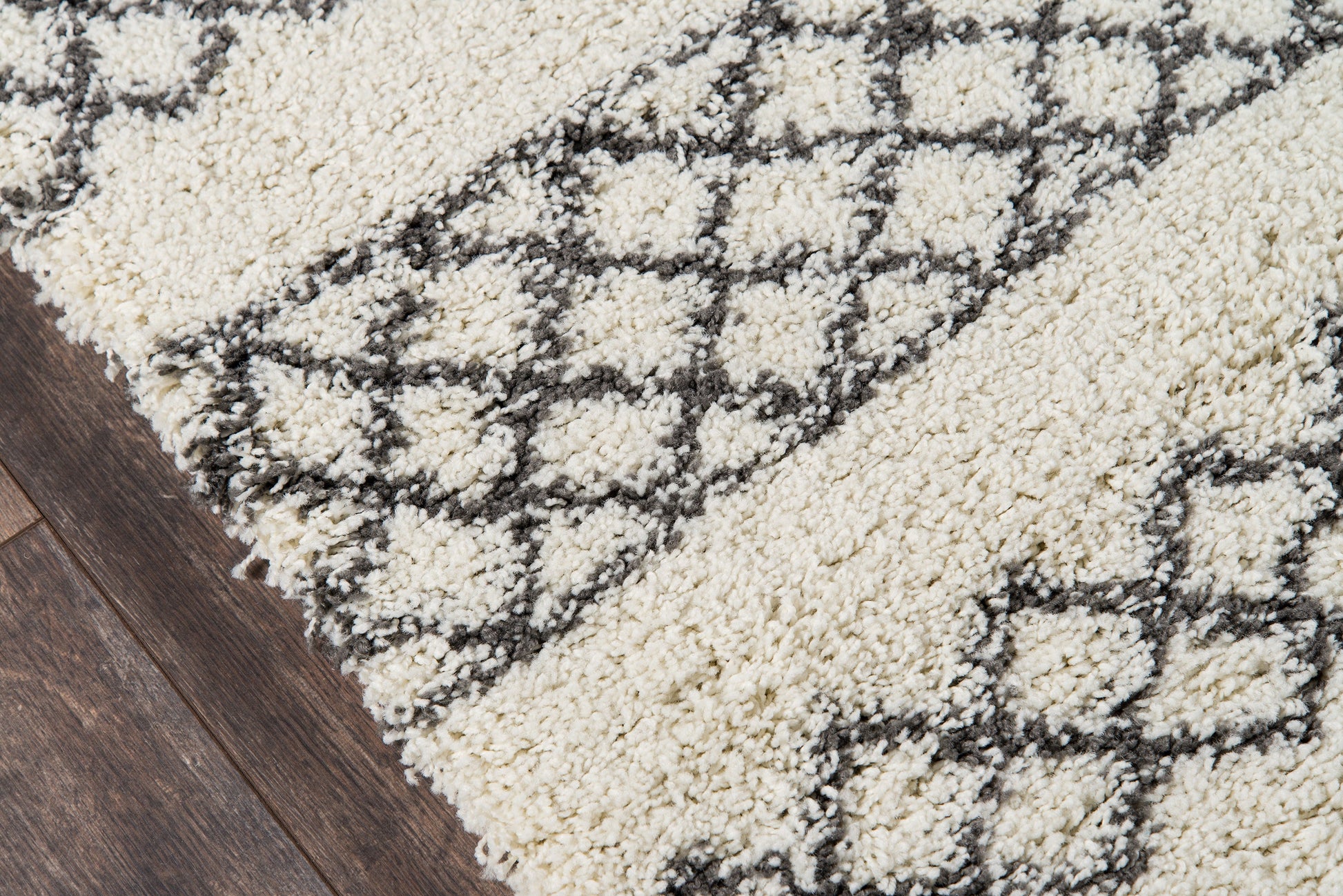 Ivory shag rug with dark gray geometric lattice pattern, plush pile on a dark wooden floor; modern Moroccan-inspired style.