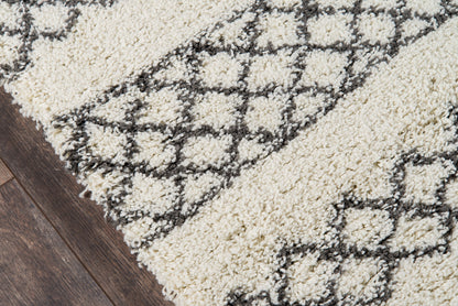 Ivory shag rug with dark gray geometric lattice pattern, plush pile on a dark wooden floor; modern Moroccan-inspired style.