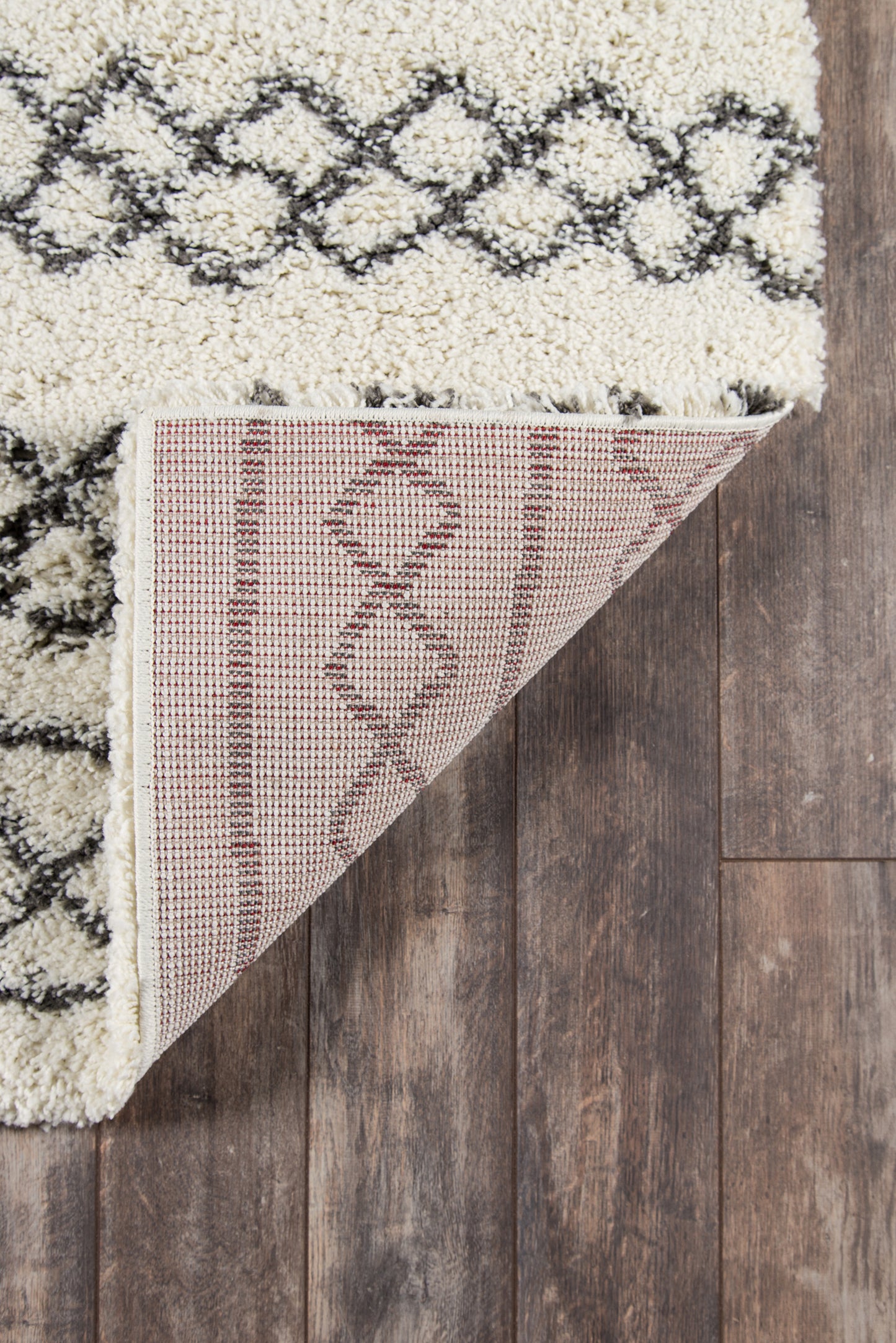 Maya Ivy ivory shag rug with black geometric lattice, underside shows pink-beige weave, on dark wood floor.