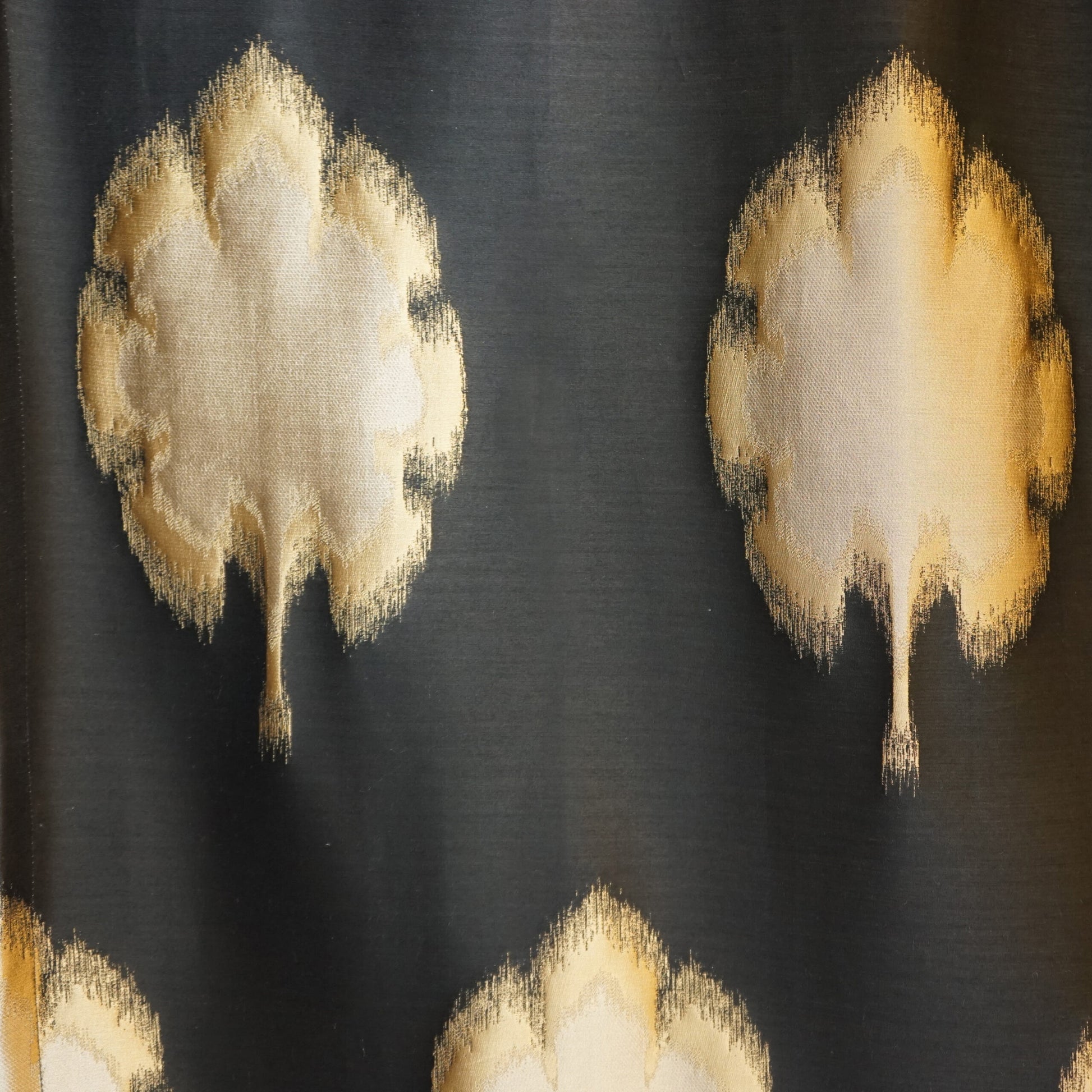 Black fabric with a repeating gold-cream and yellow Ikat jacquard pattern.