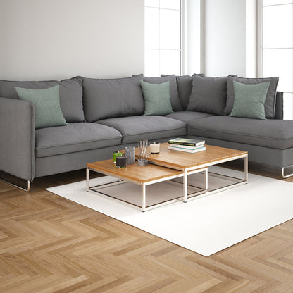 Modern gray sectional with green cushions and two-tier wooden coffee tables on a light rug in a sunlit living room.