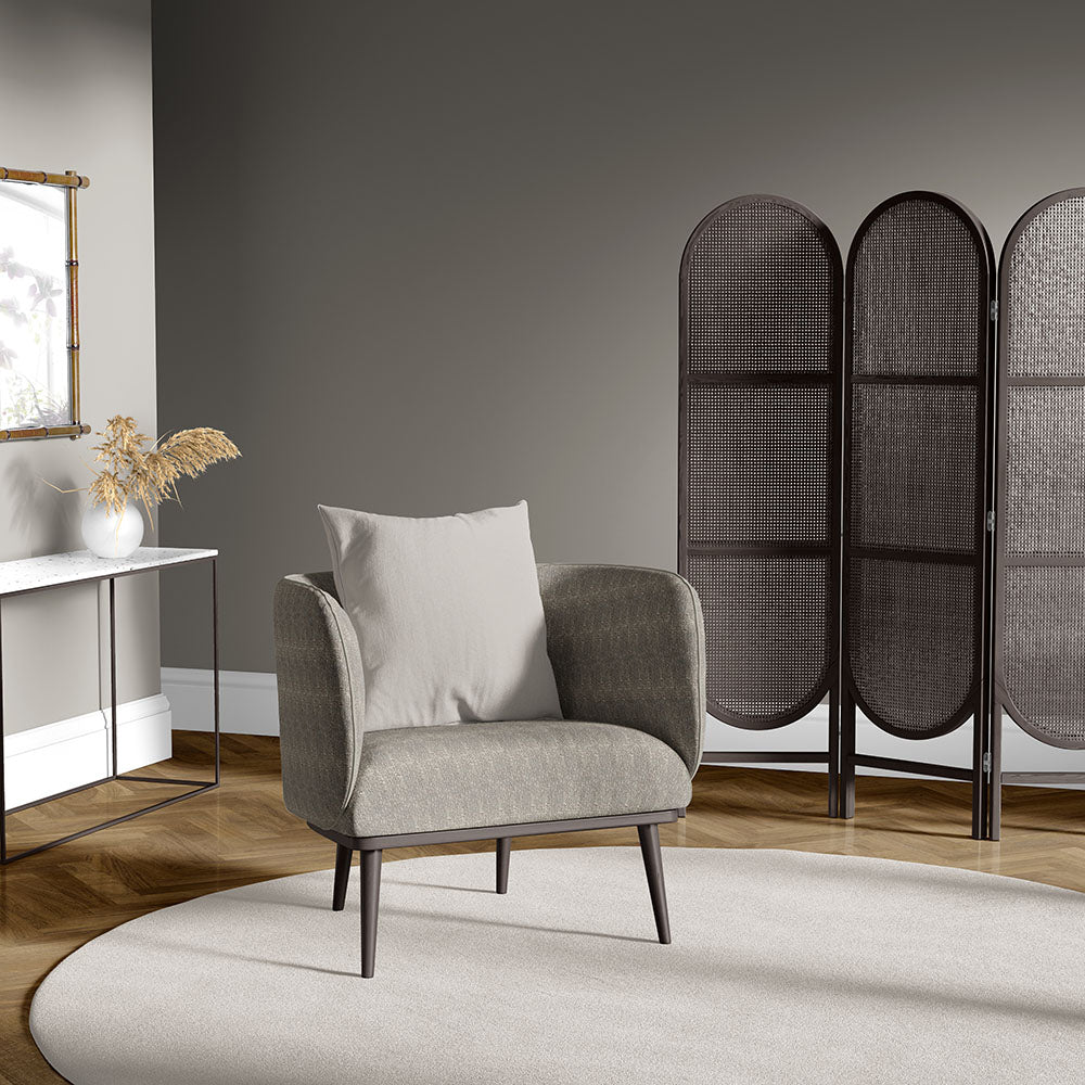 Taupe mid-century armchair with light cushion, dark legs, in grey room with a three-panel woven screen and circular beige rug