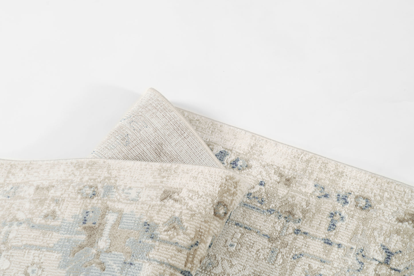 Cream-beige rug with pale blue faded pattern, woven texture, folded corner.