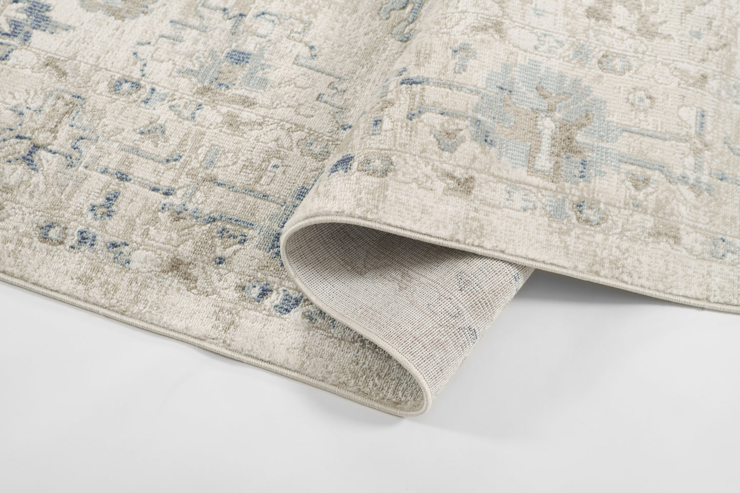 Beige area rug with faded blue oriental medallion pattern, soft plush pile; folded corner reveals underside.