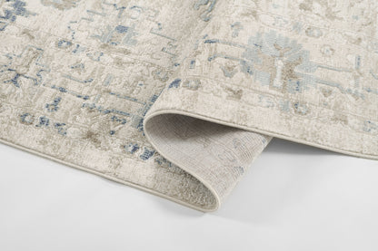 Beige area rug with faded blue oriental medallion pattern, soft plush pile; folded corner reveals underside.