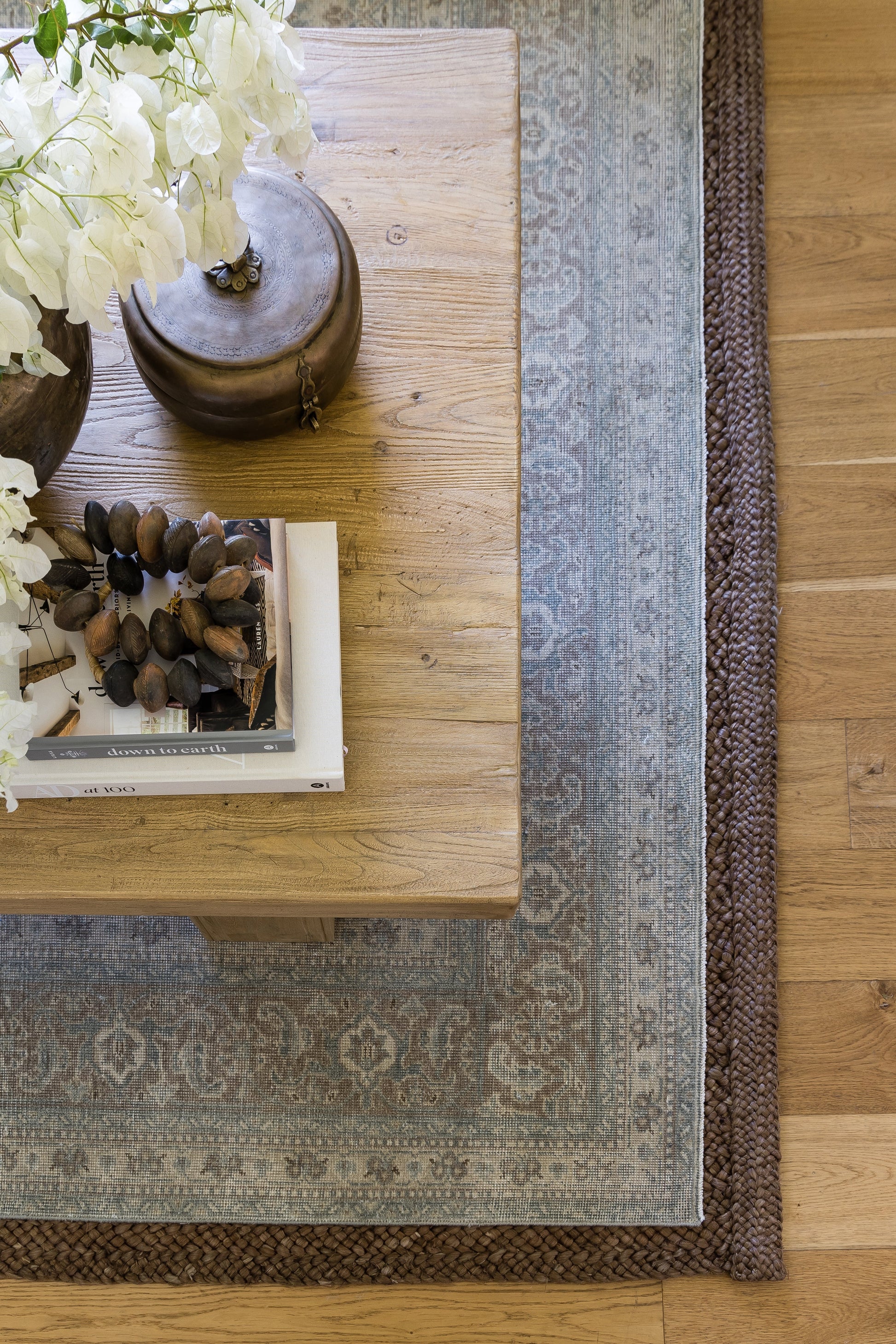Wooden coffee table with bronze kettle, white hydrangea bouquet, and stacked books on a blue patterned rug.