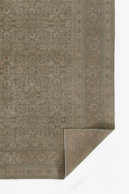 Muted blue-gray and beige oriental rug with ornate border; corner folded to reveal weave.