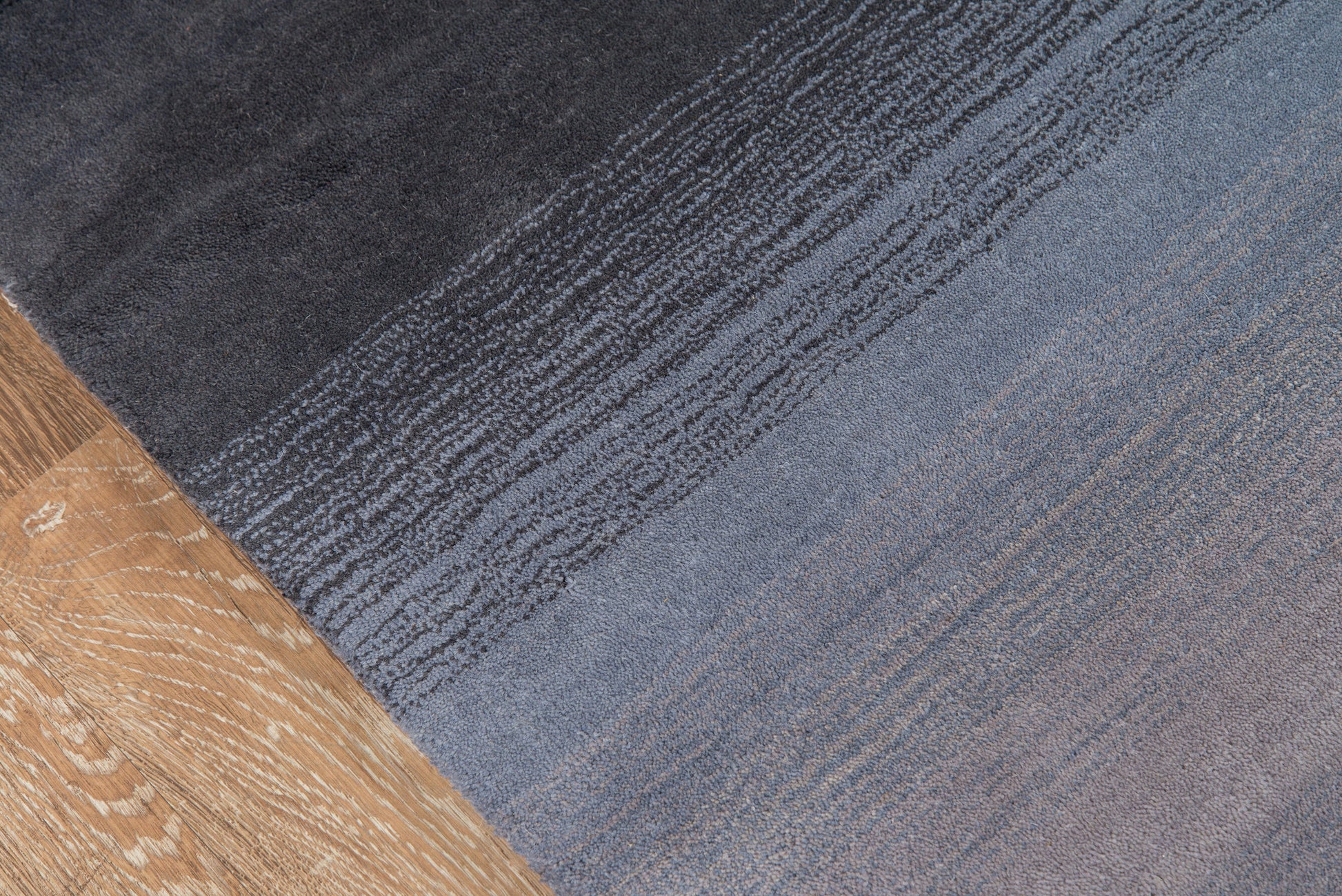 Rectangular woven rug with charcoal-to-blue gradient and subtle striped texture for modern living spaces.