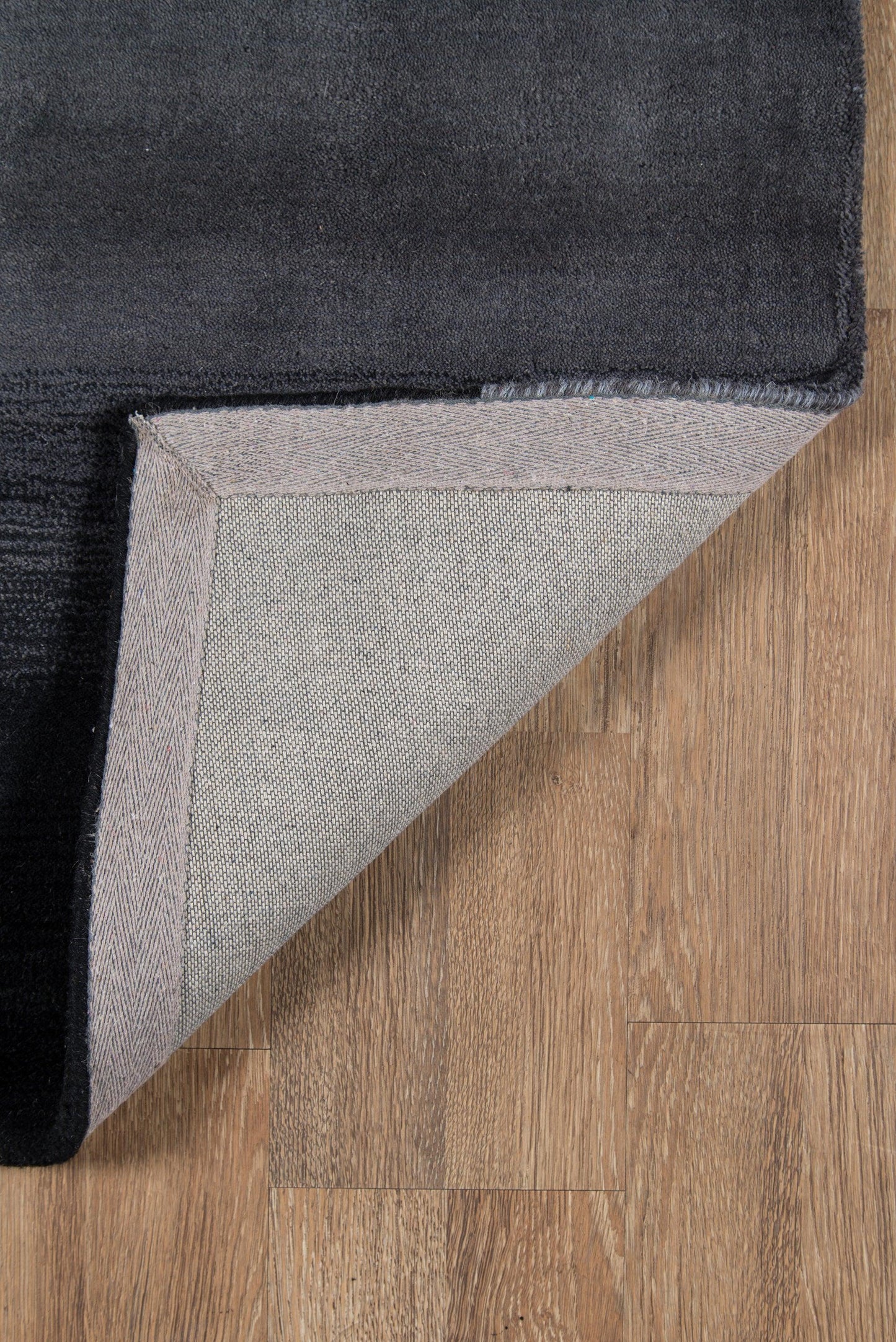 Black plush rug with light gray underside and herringbone border, folded corner on wood floor.