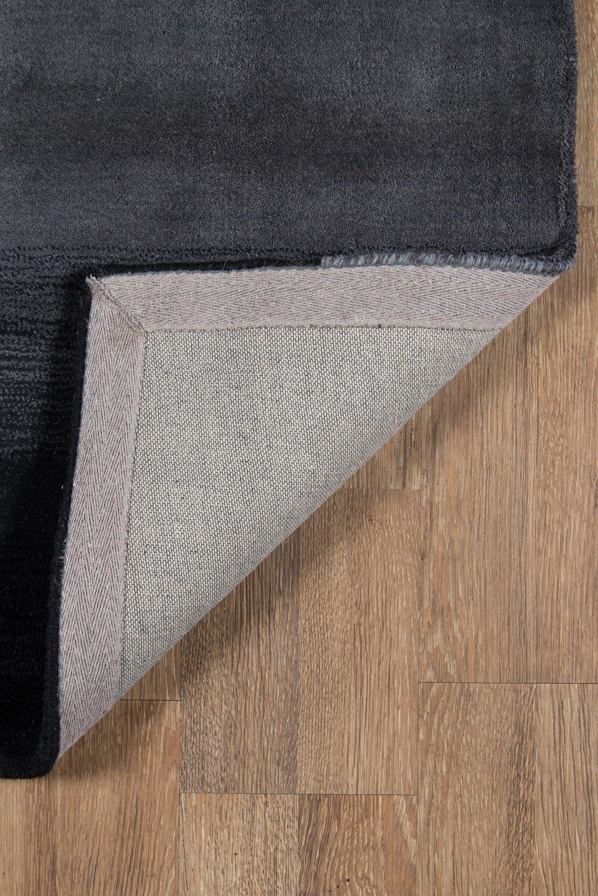 Black plush rug with light gray underside and herringbone border, folded corner on wood floor.