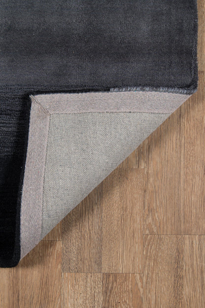 Black plush rug with light gray underside and herringbone border, folded corner on wood floor.
