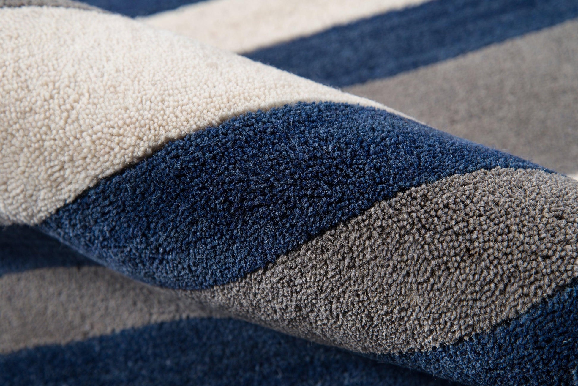 Close-up of a striped plush rug in navy, beige and gray with a thick shaggy pile.