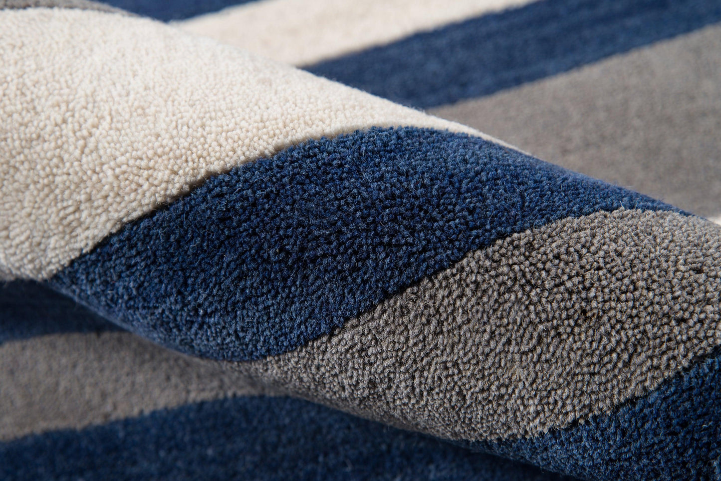 Close-up of a plush striped rug in navy, gray and beige with dense shag pile.
