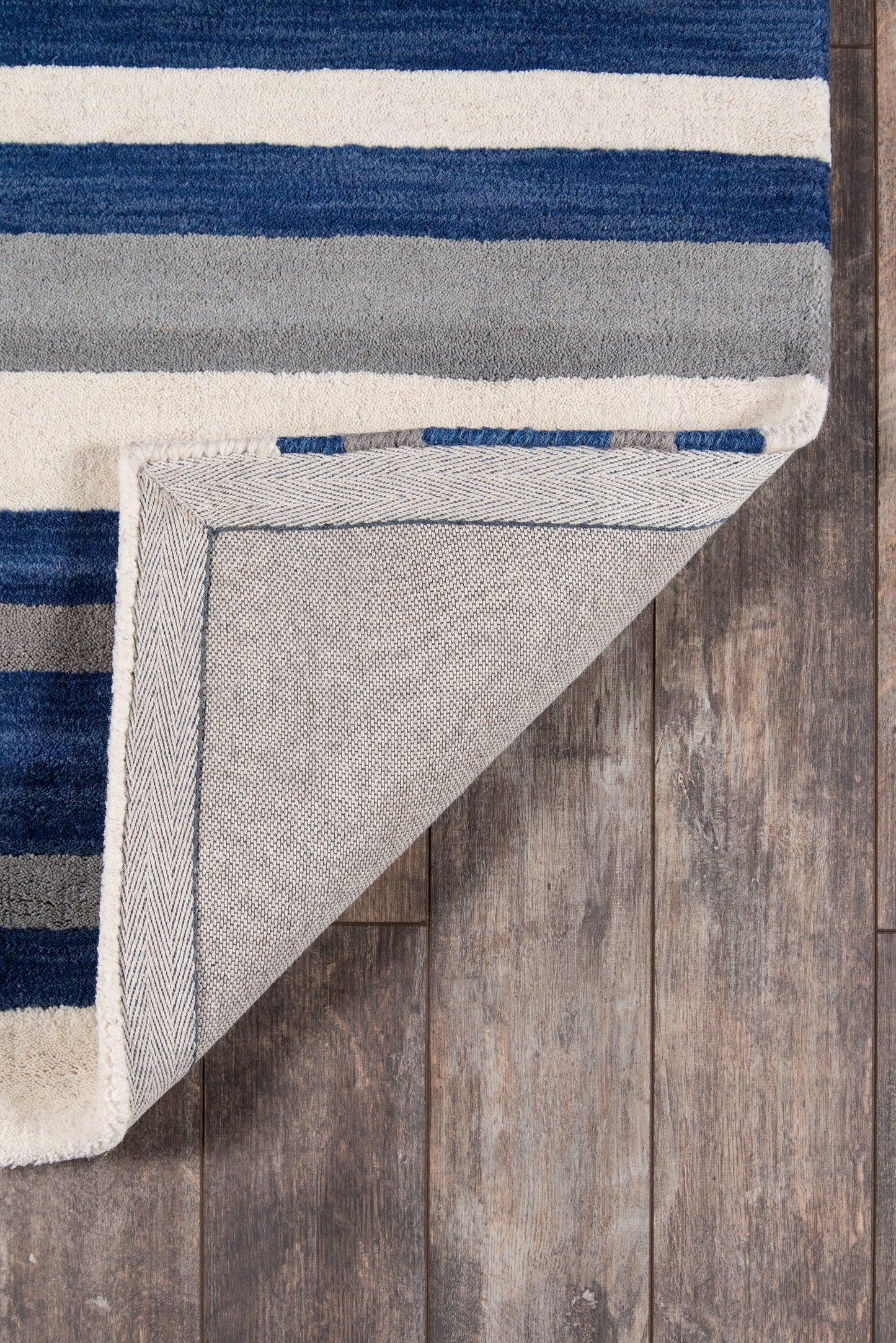 Navy blue, cream, and gray striped shag area rug; folded corner reveals light gray woven back on wood floor.