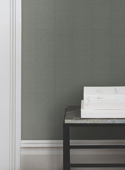 Emerald green crosshatch string wallpaper on the wall; white baseboard visible; black metal-framed side table with a speckled stone top and white books nearby.