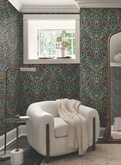 Room with black and multicolor botanical wallpaper, cream curved armchair with knit throw, window light, gold floor lamp, marble side table and standing mirror.