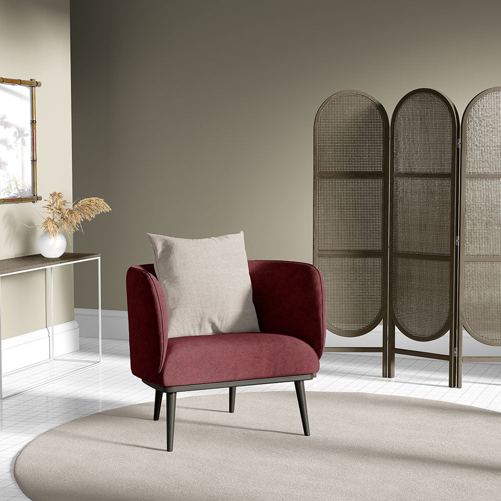 Red upholstered mid-century armchair with a beige cushion, black tapered legs on a round beige rug beside a woven folding screen.