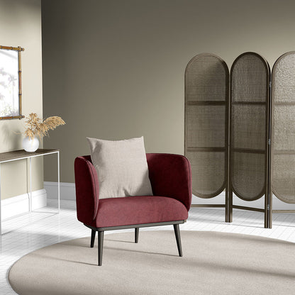 Red upholstered mid-century armchair with a beige cushion, black tapered legs on a round beige rug beside a woven folding screen.