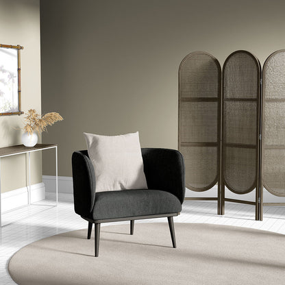 Charcoal gray mid-century armchair with a light beige cushion on a round beige rug beside a wicker folding screen.