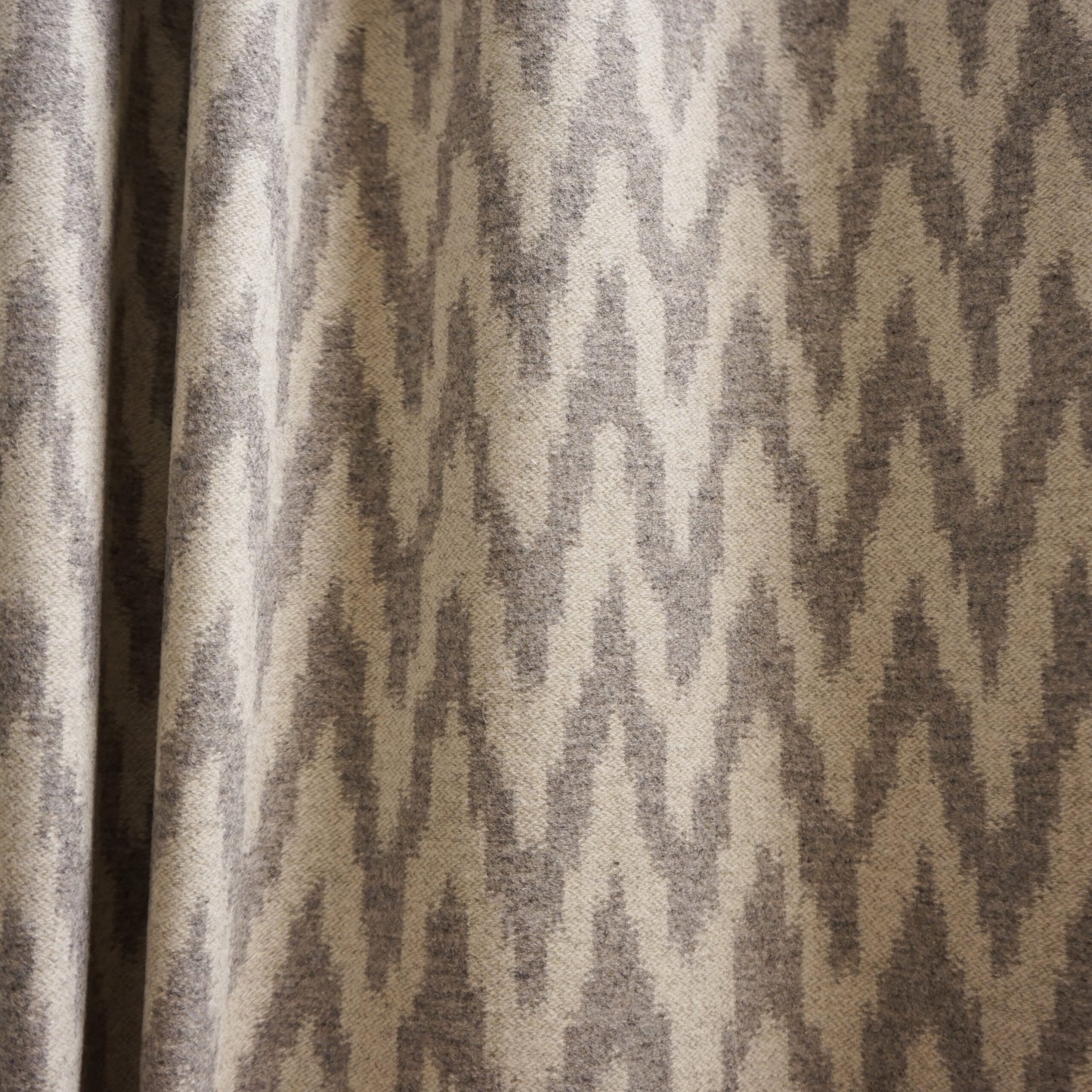 Beige and taupe ikat-patterned curtain fabric with soft texture and draped folds.