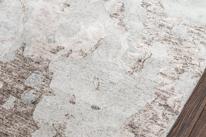 Light gray area rug with tan-brown abstract pattern and textured pile over dark wood flooring.