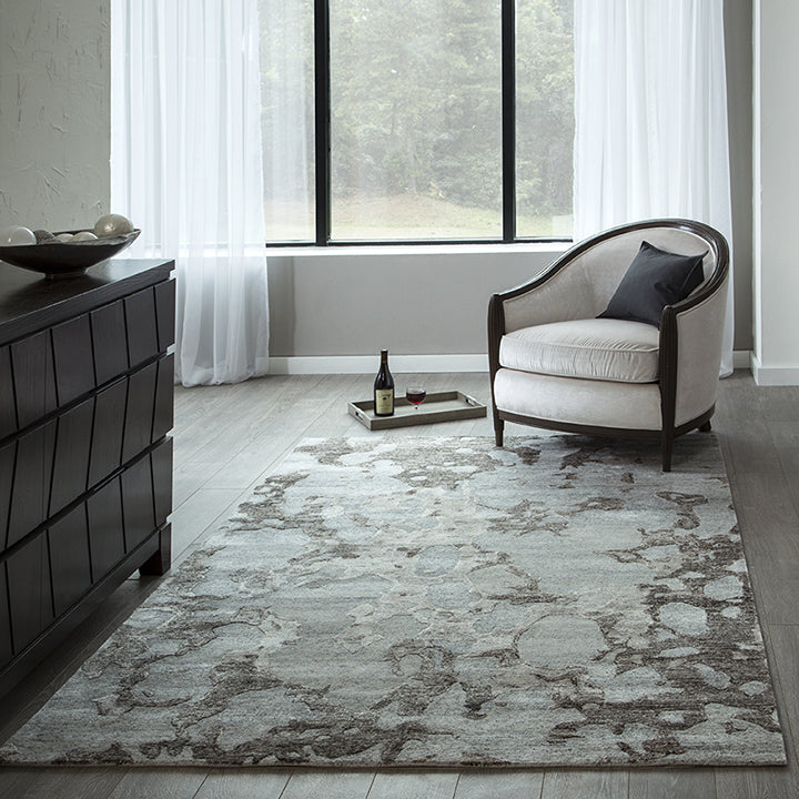 Gray abstract patterned area rug in modern living room with cream armchair and dark wood dresser