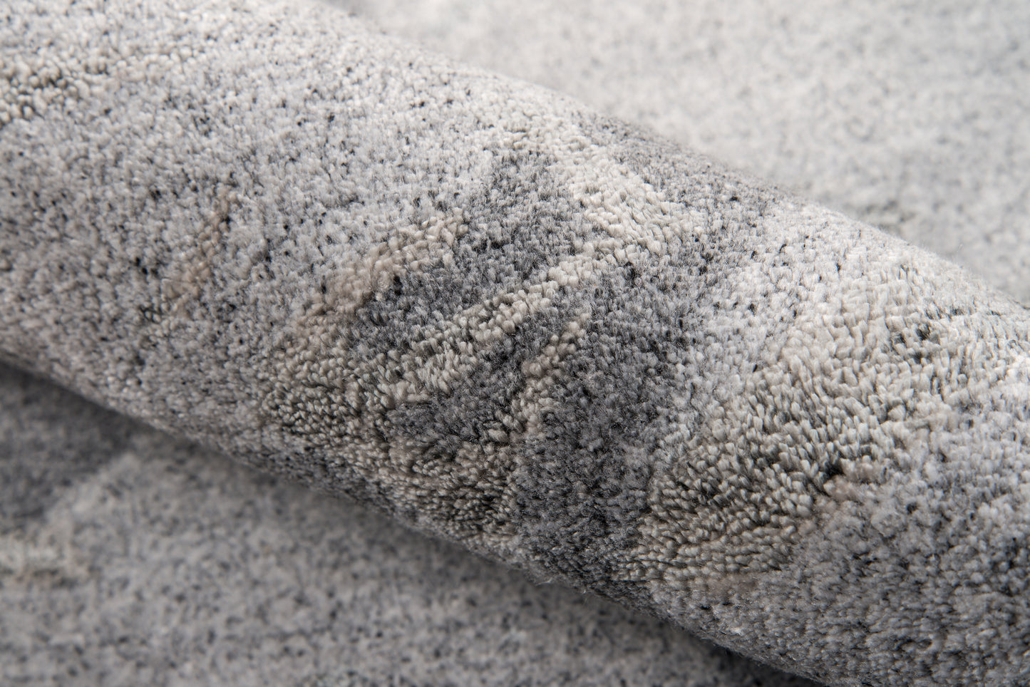 Grey shag rug, rolled view showing soft plush high-pile texture in mottled light and dark grey tones.