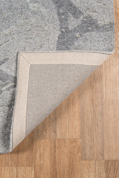 Gray patterned area rug with beige underside, folded corner showing woven backing on a wood floor.