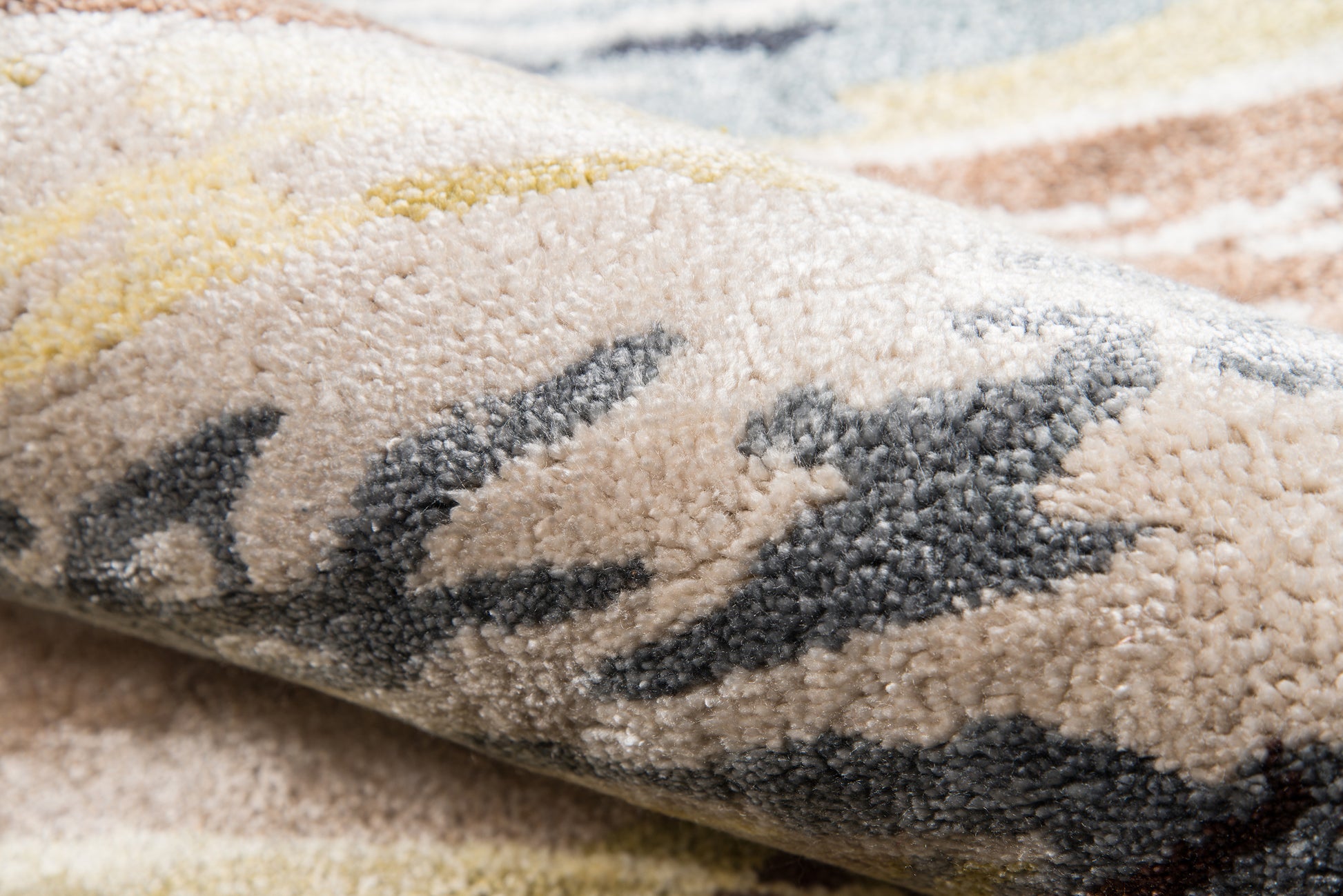 Close-up of a plush multicolor rug with beige base and dark gray abstract pattern, textured fluffy pile.