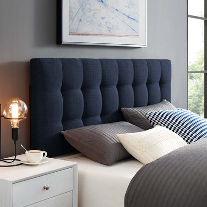 Navy tufted headboard with gray quilted bedding, white patterned cushions, white nightstand, Edison lamp.