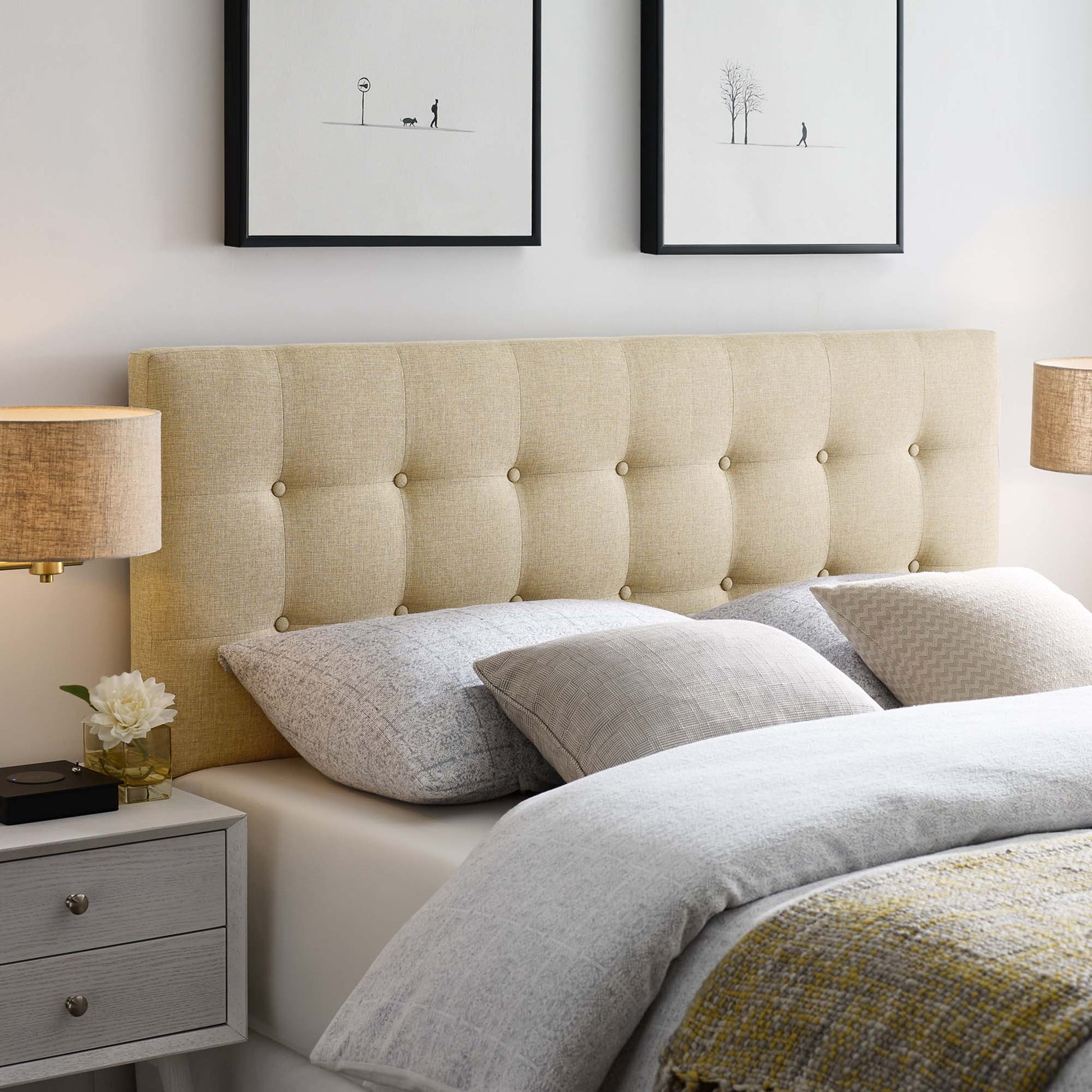 Beige tufted upholstered bed headboard with gray linens, matching nightstands, warm lamps, and minimalist framed art.