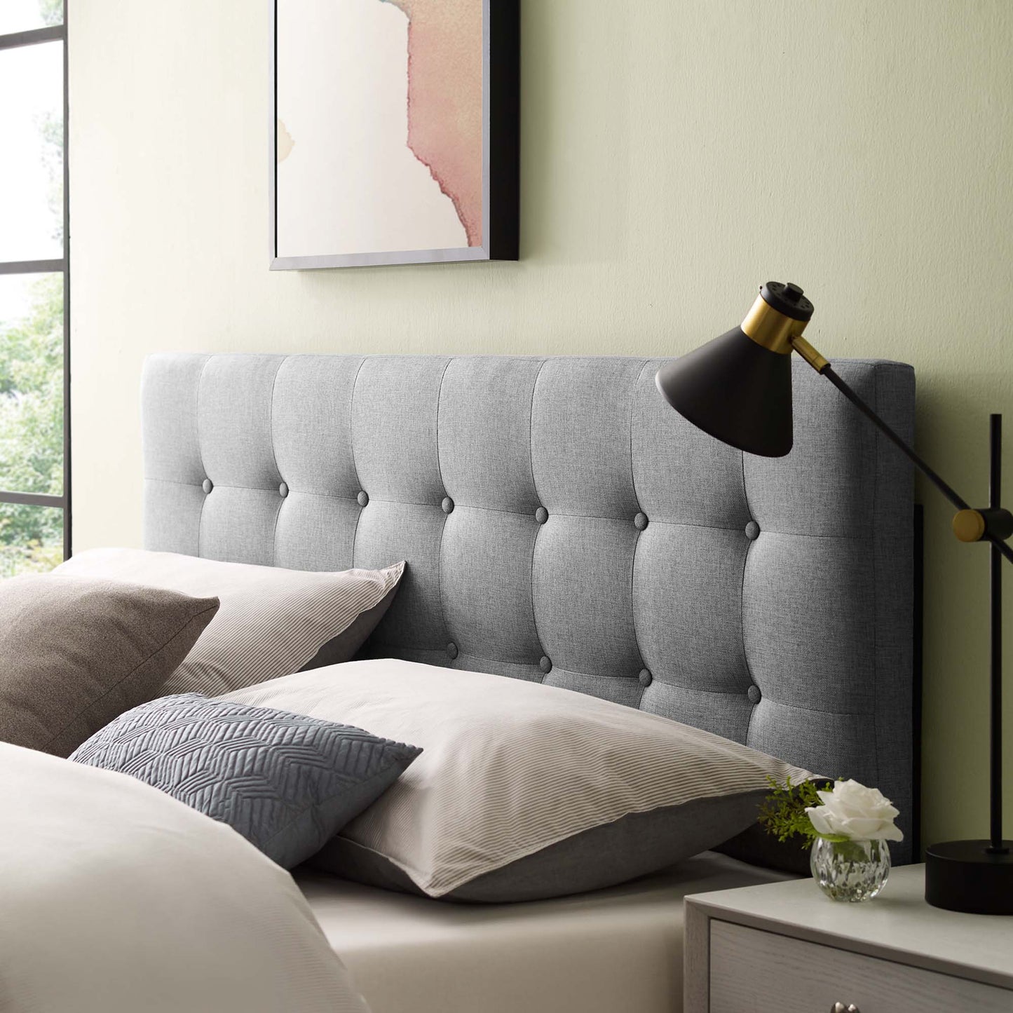 Gray tufted fabric queen headboard with neutral bedding and pillows, black brass adjustable lamp, nightstand with vase, sage wall.