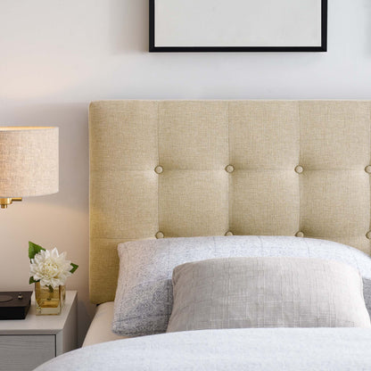 Brown tufted upholstered headboard with button details, light gray bedding, & bedside table with lamp and white flowers.