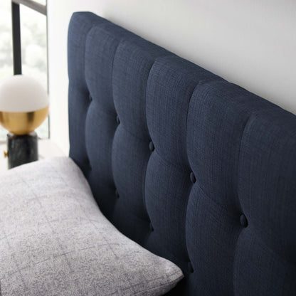Navy blue tufted fabric headboard with button details beside a light gray quilt and gold bedside lamp.