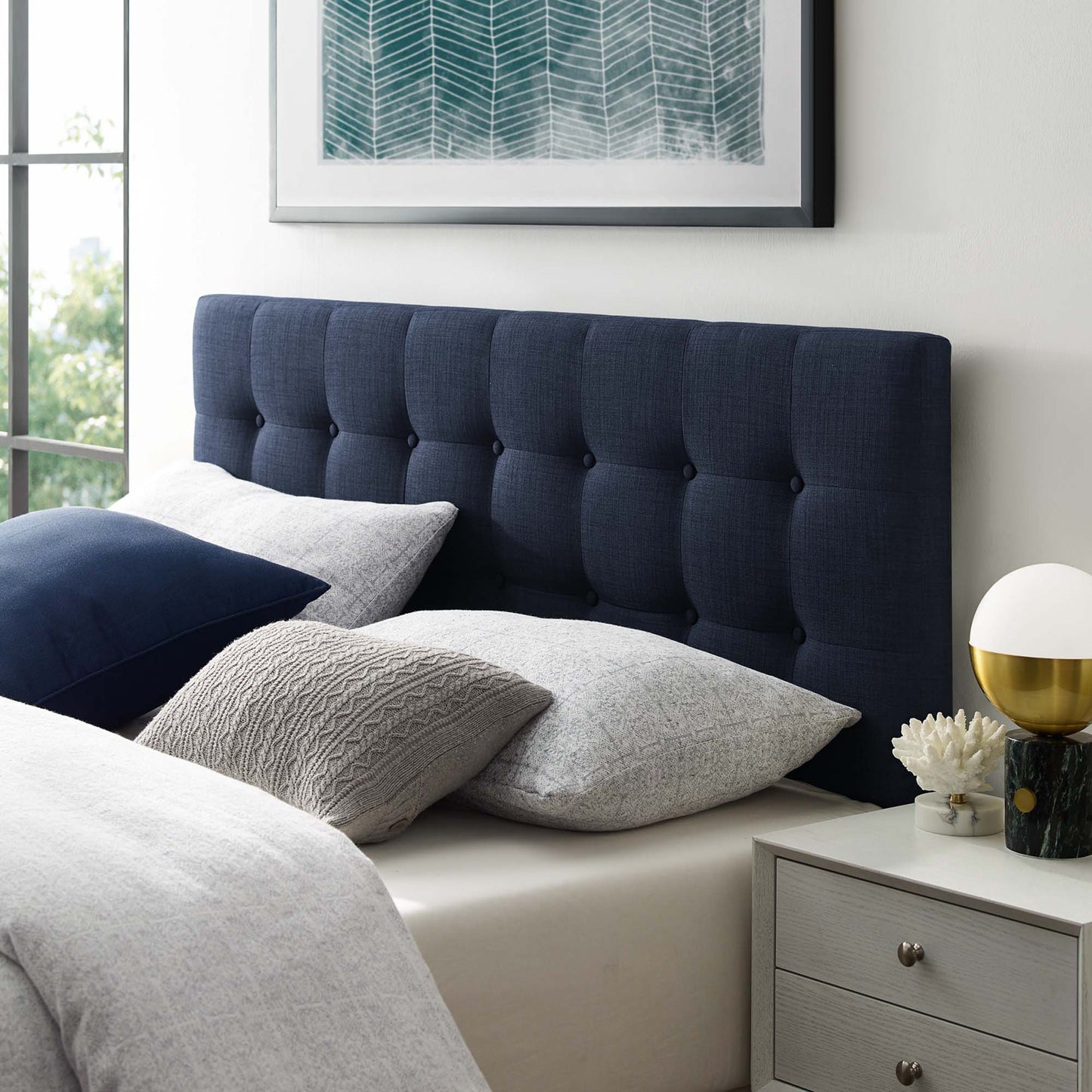 Navy tufted king fabric headboard with gray and white bedding, teal art above, and a nightstand with a white globe lamp and gold base.