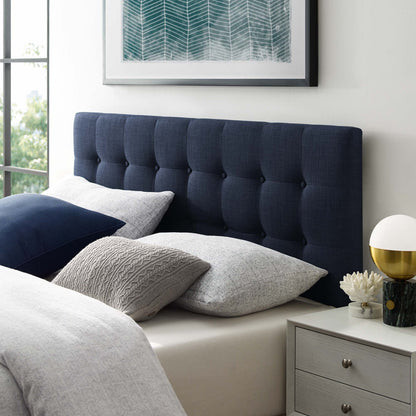 Navy tufted king fabric headboard with gray and white bedding, teal art above, and a nightstand with a white globe lamp and gold base.