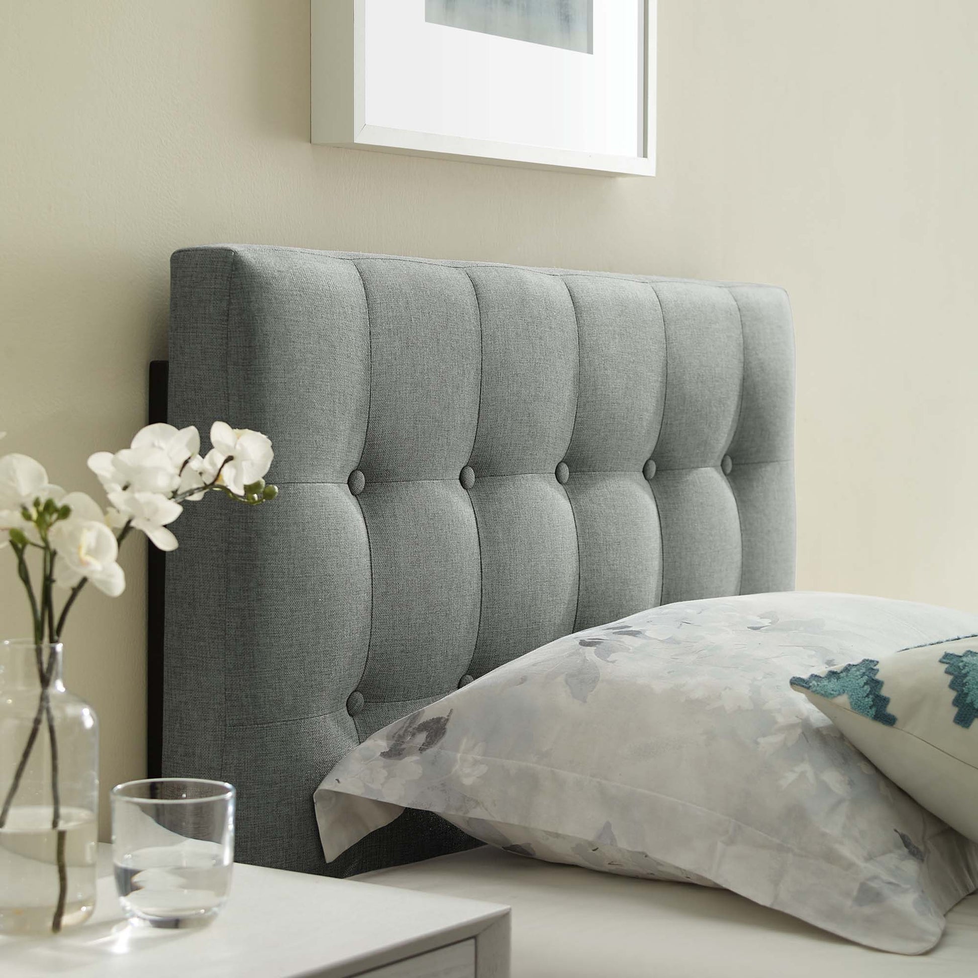 Tufted gray fabric twin headboard with vertical channels, shown on a modern bed with a white nightstand and a vase of white flowers.