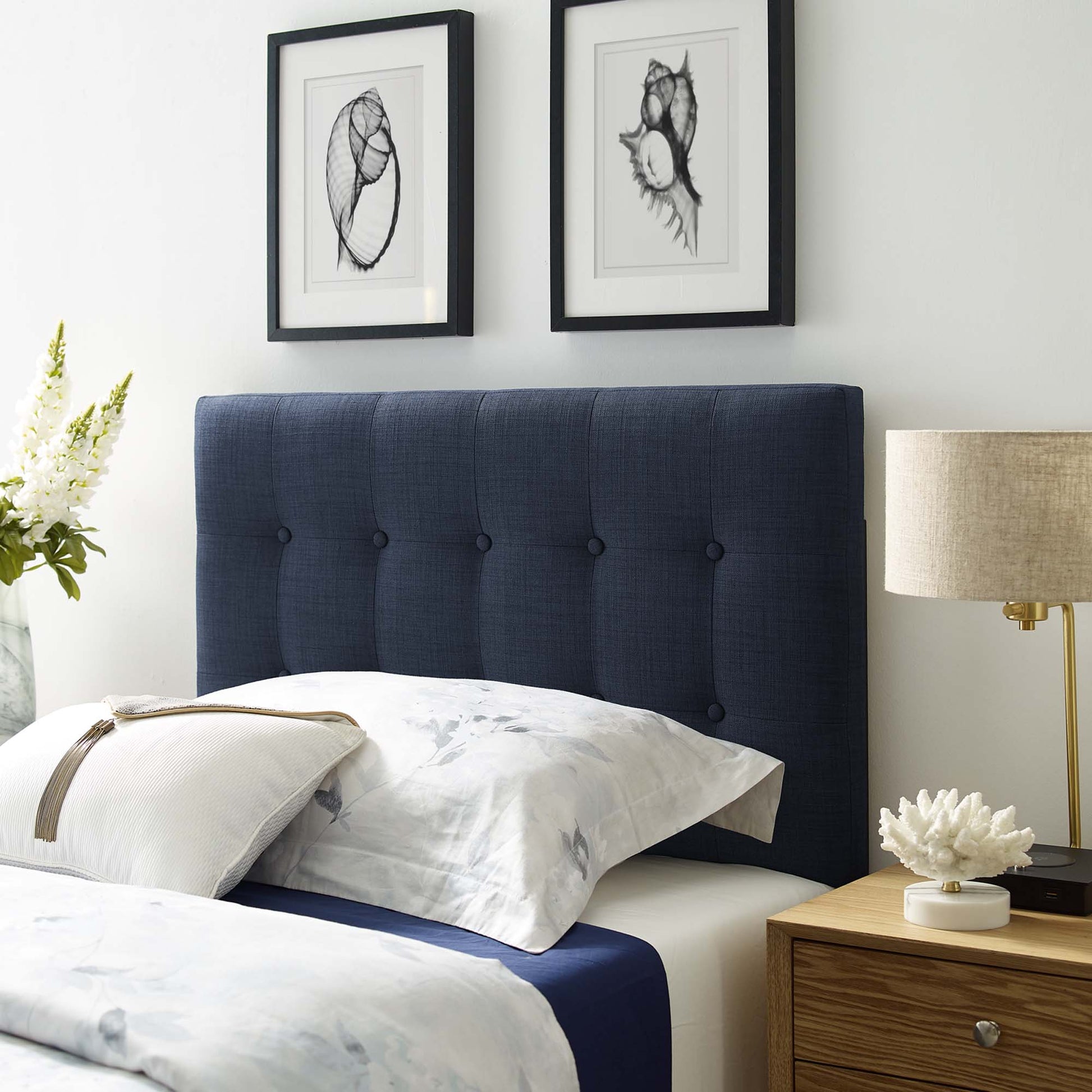 Navy tufted upholstered twin headboard with white-and-blue bedding; two framed botanical prints above; wood nightstand with lamp.