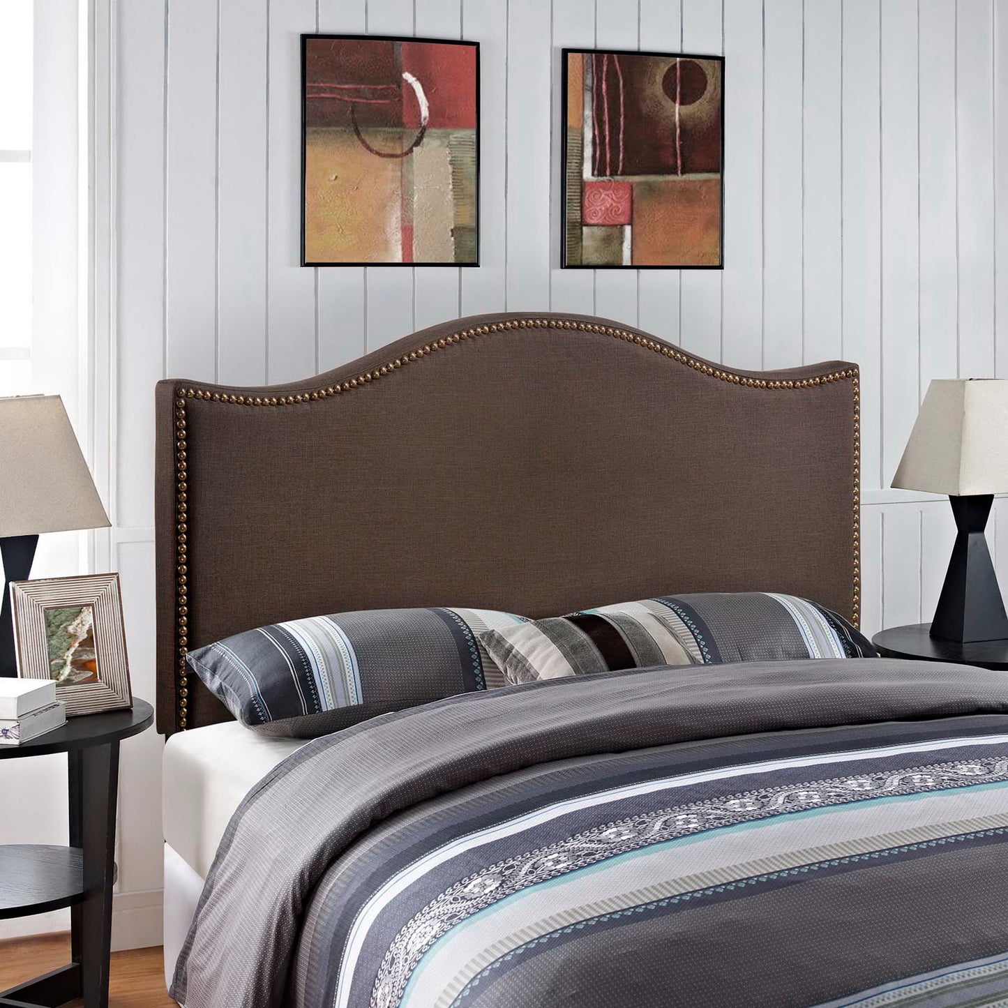 Dark brown upholstered queen headboard with a curved silhouette and brass nailhead trim; blue-gray striped bedding visible in a contemporary bedroom.