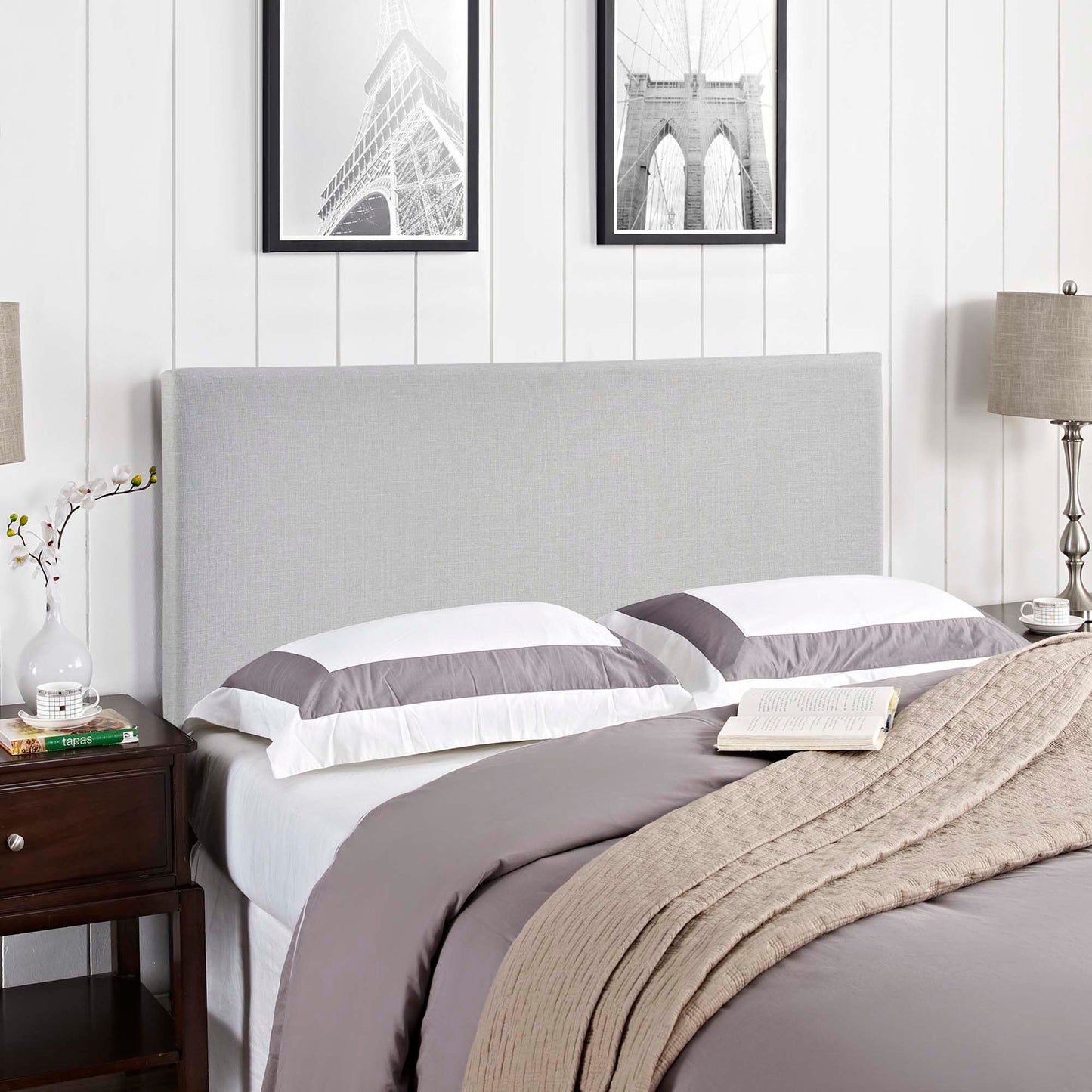 Gray upholstered headboard with white and gray bedding, beige knit throw; dark wood nightstands and framed monochrome art.